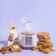 Load image into Gallery viewer, Packaged Dam Good English Muffins with cinnamon swirl, a mug of coffee, and cinnamon sticks on a purple background.
