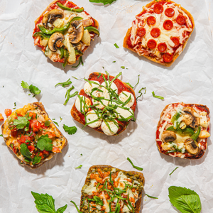 Assorted small Dam Good English Muffin pizzas on a white surface with fresh herbs.
