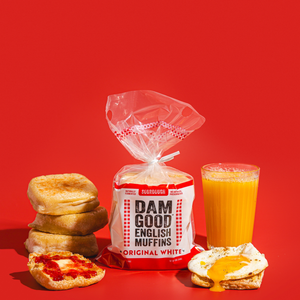 Bag of Dam Good English Muffins with a glass of orange juice and muffins on a red background