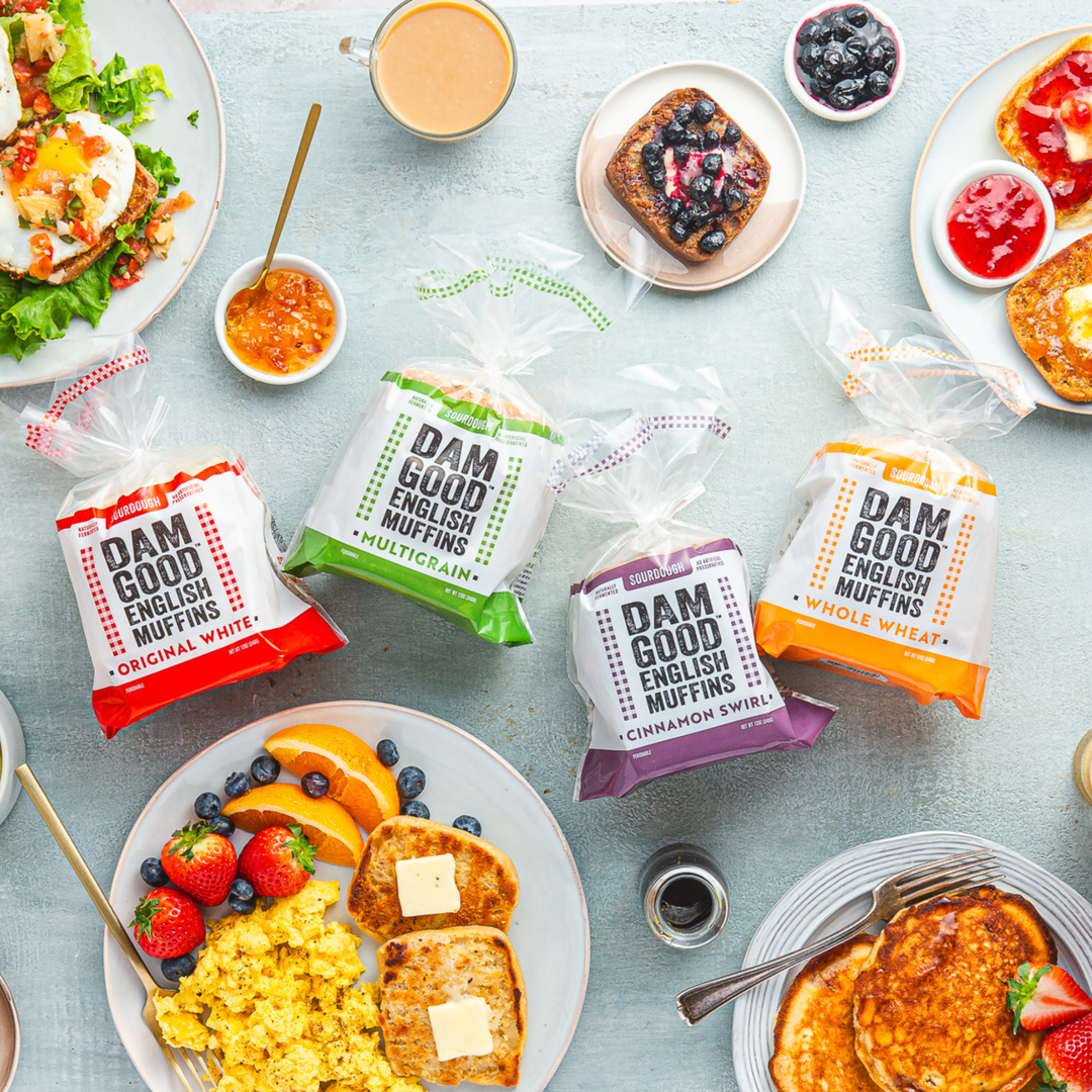 Assorted packages of 'Dam Good English Muffins' on a table with breakfast items.
