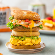 Load image into Gallery viewer, Stacked English muffin breakfast sandwiches with egg and avocado on a plate with a blurred background
