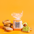Load image into Gallery viewer, Packaged Whole Wheat English muffins with a sliced avocado on toast against an orange background
